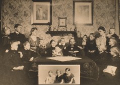 Schwarz-weiß Foto mit Großfamilie sitzend um einen Tisch vor Wand mit Fotos