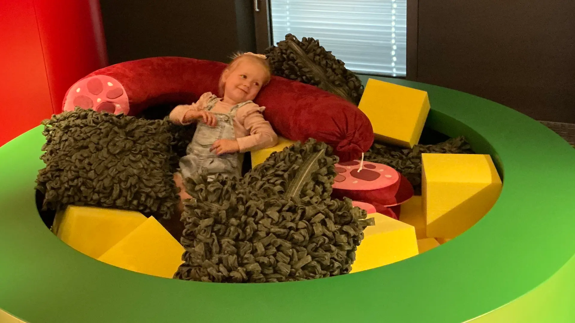 Das Bild zeigt ein Kind, das im Stamppot sitzt, der mit grünem Gemüse, einer Wurst und Käsewürfeln aus Styropor gefüllt ist